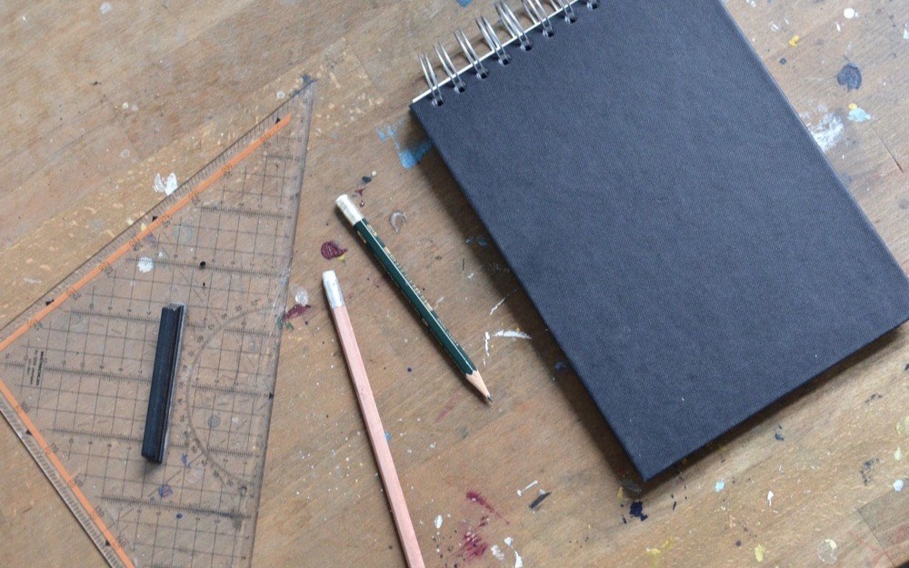 A notebook and marking pencils on a work surface